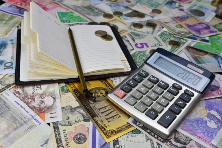 calculadora com moedas e notas ao fundo